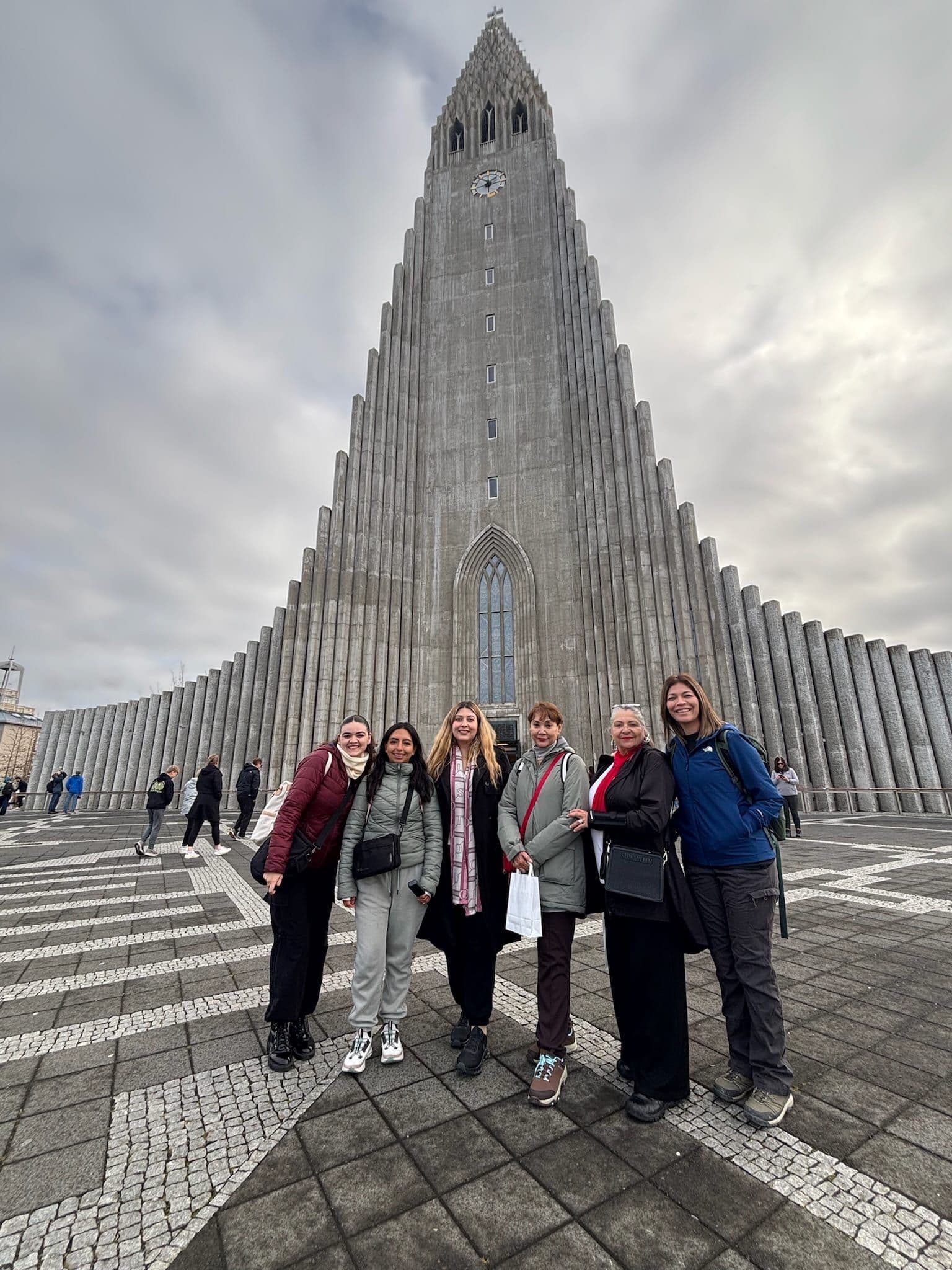 Seis viajeras de un grupo Flymingo Women posando juntas frente a la iglesia Hallgrímskirkja de Reikiavik, abrigadas en un día nublado.