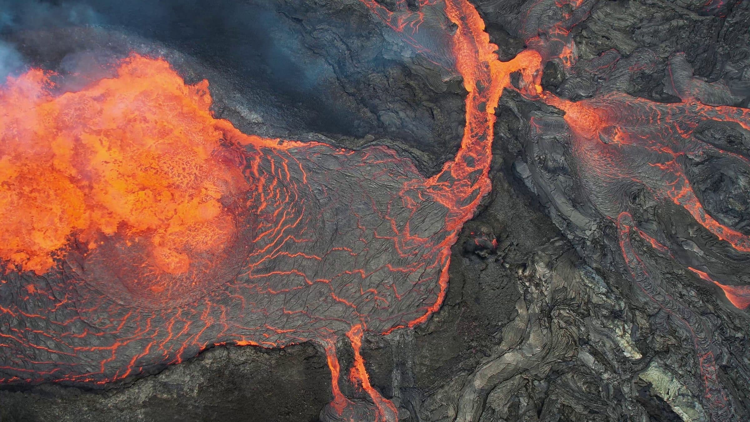 Vista aérea de una fisura volcánica islandesa con ríos de lava incandescente abriéndose paso sobre un campo de lava negra.