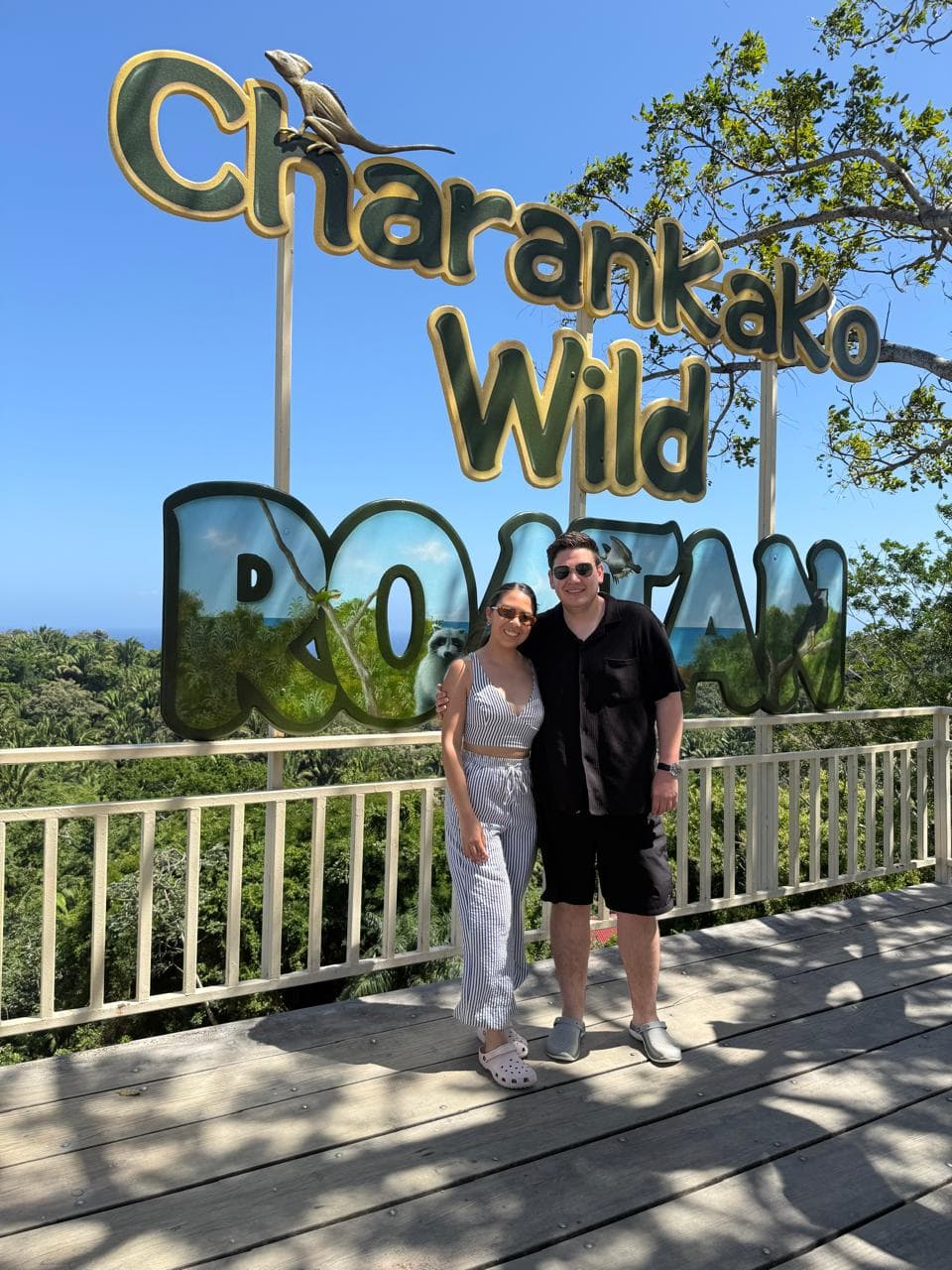 Sergio y Alexia frente al letrero de Charankako Wild Roatán, rodeados de vegetación tropical.