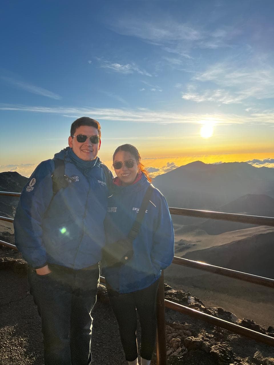 Sergio y Alexia con chamarras azules al amanecer, en lo alto de un volcán y por encima de las nubes.